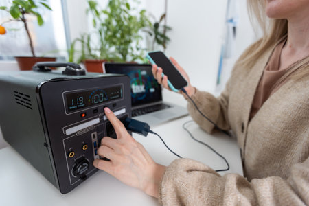 Mobile phone charging on wireless pad and woman using laptop on wooden backgroundの写真素材