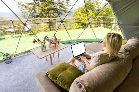 Young caucasian woman using and watching on laptop computer on in dome camping hotel. Tourism, vacation and weekend.の写真素材