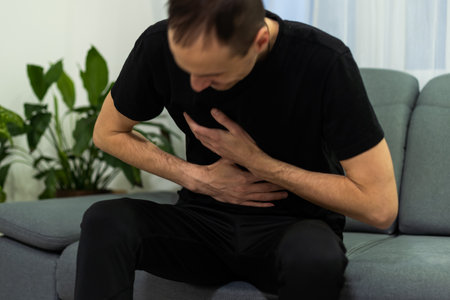 Man suffering with severe stomach pain sitting at home. Hand of mature guy holding abdomen suffering from ache, diarrhea or indigestive problem. Caucasian guy pressing on belly on painful sensationの写真素材