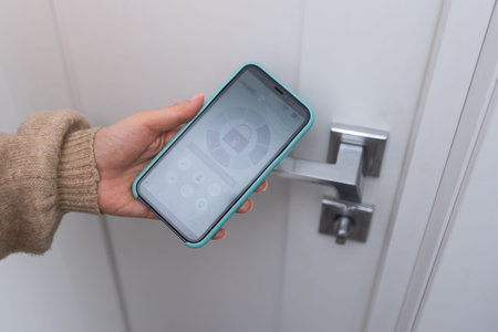 Close-up of woman controlling the security of her house with mobile app on smartphone, she locking...
