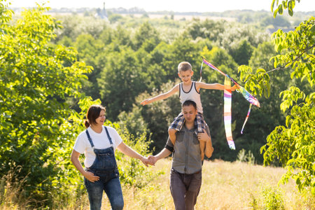 Happy family with pregnant wife fly a kite together in summer fieldの写真素材