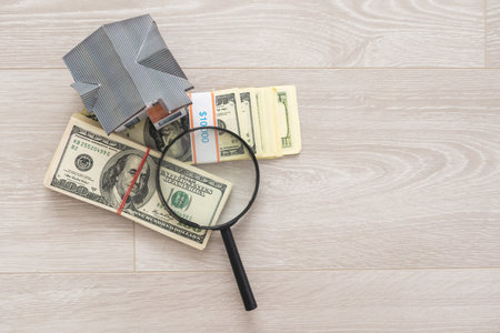 Model of house with magnifying glass and money on white.の写真素材
