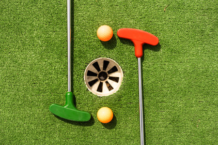 Mini-golf clubs and balls of different colors laid on artificial grass.の写真素材