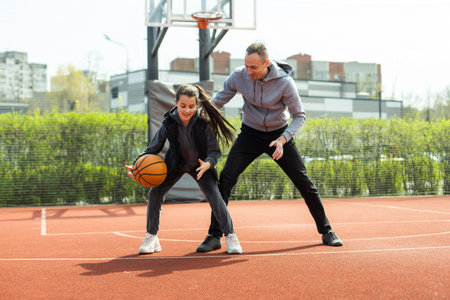 Happy father and teen daughter outside at basketball court.