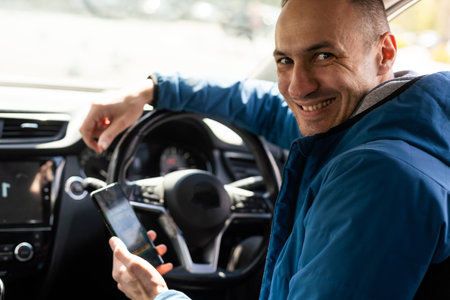 Close up cropped shot of man hand holding mobile phone with bookmaker;s website on its screen. Male gambler betting online using mobile application white sitting in a car.の写真素材