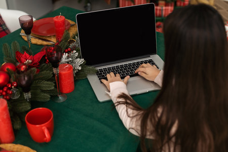 Cute girl using computer by christmas treeの写真素材