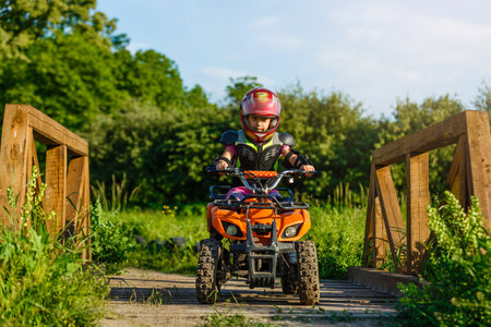 The little girl rides a quad bike. A mini quad bike is a cool girl in a helmet and protective clothing. Electric quad bike electric car for children popularizes green technologyの写真素材