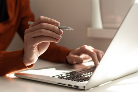 Work from home office, teleworking, online learning concept. Businessman typing on laptop computer at home. Man browsing internet at home. Student studying online class with pen, book on desk, closeupの写真素材