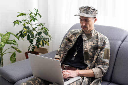 partial view of army soldier using laptop on couchの写真素材
