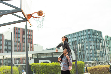 Father Carrying Daughter On Shoulders Helping Her To Put Basketball In Netの写真素材