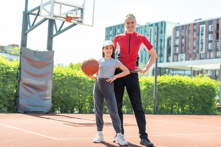Happy father and teenage daughter playing basketball outside at courtの写真素材