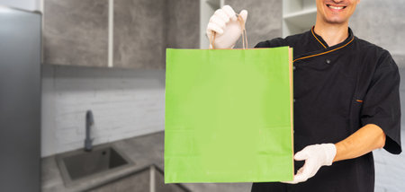 Paper pocket and food containers in hands of a smiling deliveryman. Quality service of a restaurant.の写真素材