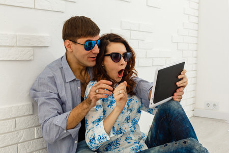 Portrait of a cheery happy couple holding tablet while standing and celebrating isolated over gray wall backgroundの写真素材