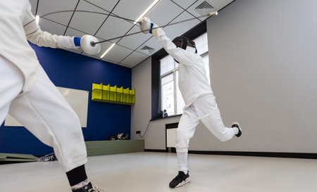Adults and teens wearing a fencing uniform practicing with foil in the gymの写真素材