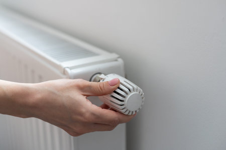 A womans hand holds the heating thermostat handle. Heating service cost concept, utility price...