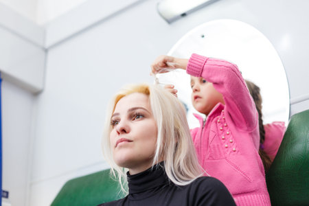 a little girl does her mothers hair while playing together. childrens entertainment for mothers and daughtersの写真素材