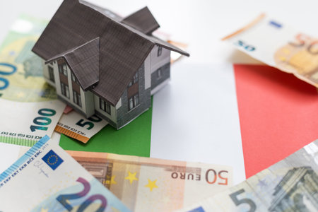 A model of a small white house on a background of Euros banknotes.