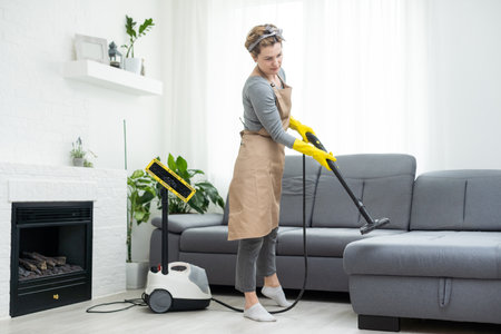 Woman cleaning couch with vacuum cleaner at homeの写真素材