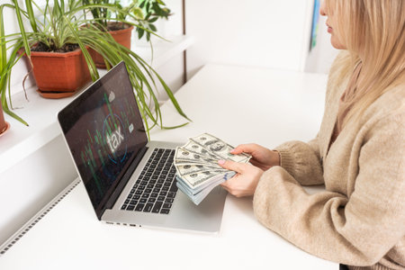 Close up rear view young woman using laptop and money, checking financial documents, sitting at table at home, computer screen with diagrams,の写真素材