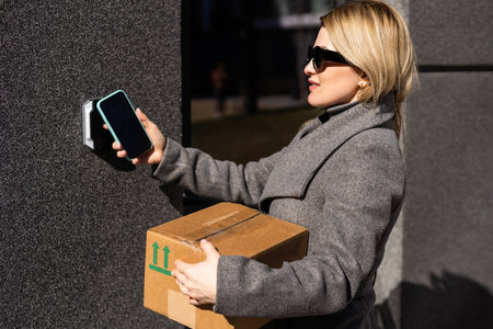 Smart home concept - close up of woman with box use mobile phone to open electronic lockの写真素材