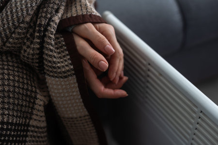 Woman warming hands near heater indoors, closeup