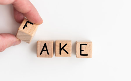 The word fake written on wooden blocks, a man sitting in front of his desk with a pen and notebook on itの写真素材