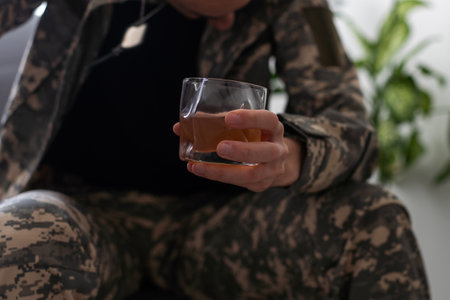 Serious anxious and nervous military man suffers from depression while sitting alone at home. Pensive man in military uniform sitting on sofa propping his head with his hands. PTSD concept.の写真素材