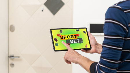 Cropped shot of male fan making bets using gambling mobile application on his phone. Man watching football play online broadcast on his laptop waiting for winning results. Bet wins.の写真素材