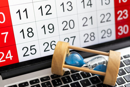 Small hourglass stands on the calendar, counting the time. The concept of the deadline of projects,...