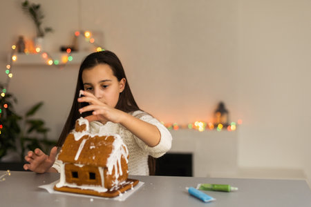 Kids baking Christmas gingerbread house. Children celebrating winter holiday at home. Decorated living room with fireplace and tree. Family activity. Little girl making cookiesの写真素材