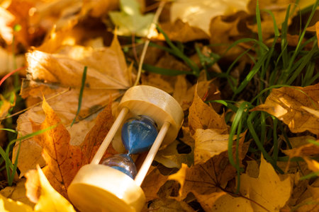 Hourglass and autumn leaves in the park. A symbol of passing time. Symbol of short life.