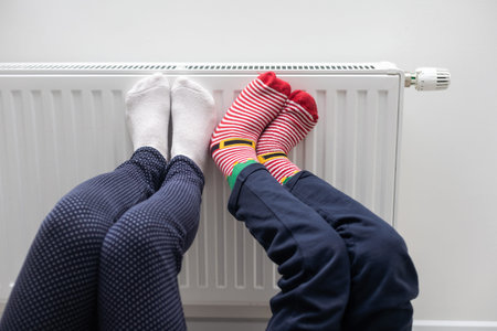 Mother and child warming feet near heater at home, closeup