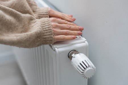 Female hands are trying to keep warm on an aluminum radiator. A woman warms herself near a radiator in winter during the energy crisis in Europe.の写真素材
