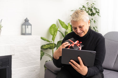 Smiling middle-aged Caucasian woman sit on couch in living room browsing wireless Internet on tablet, happy modern senior female relax on sofa at home using pad device, elderly technology conceptの写真素材