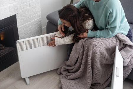 Mother and child warming hands near electric heater at home, closeup.の写真素材