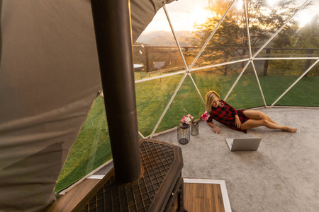 Happy young woman chatting online by using laptop in dome camping. Glamping vacation conceptの写真素材