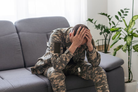 Having flashbacks. Post traumatic stress disorder. Soldier in uniform sitting indoors.の写真素材