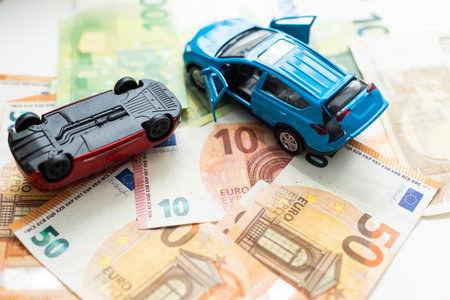 The concept of receipt of insurance premium after car accident: two toy cars and a stack of Russian rubles in the banking package lying on the background of scattered banknotesの写真素材