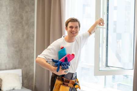 Side view of smiling man with bottle of detergent and rag cleaning window at homeの写真素材