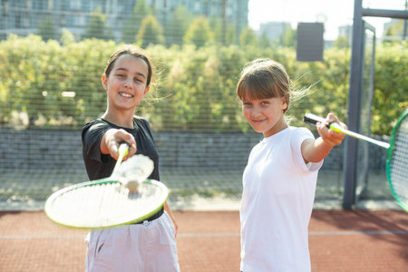 Happy sporty elementary school age girl, child playing badminton, holding a racket making funny faces, portrait, lifestyle. Sports, exercise and healthy outdoor activities leisure concept, one personの写真素材