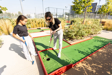 Mother and her little daughter practicing to hit the ball at the course