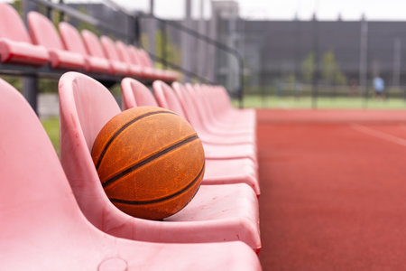 Used basketball in the foreground lies on an empty basketball court with a blurred background.の写真素材