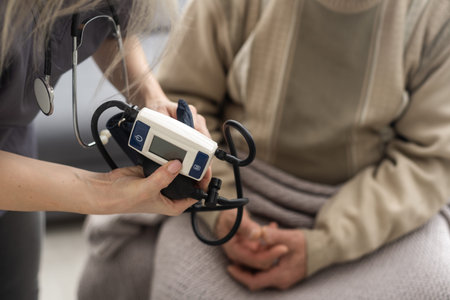 Young woman doctor wearing white uniform with stethoscope checking mature patient blood pressure at...