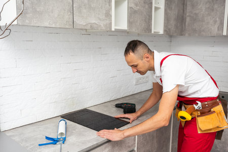 thoughtful adult repairman repairing electric stove at kitchenの写真素材