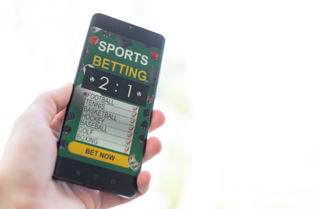 Man betting on sports using smartphone and laptop at table, closeup. Bookmaker websites on displays