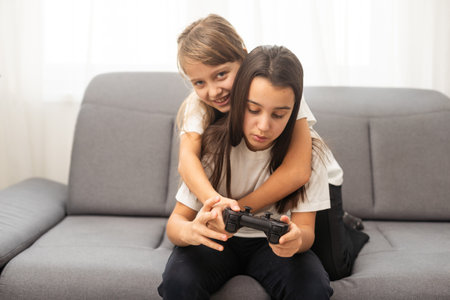 Two little girlfriends playing video game with joysticks. Excited and focused european children. Childhood concept. Entertainment and leisure. Idea of friendship. Grey background in studio. Copy spaceの写真素材