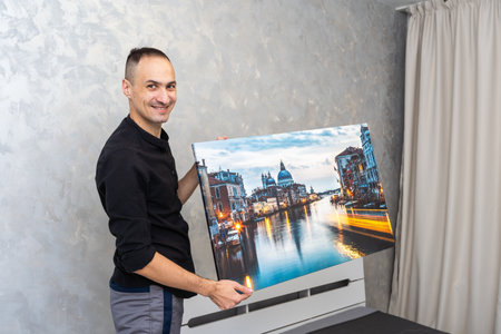 Good-looking adult artist in his 30s is about to hang a colorful little painting in the wallの写真素材