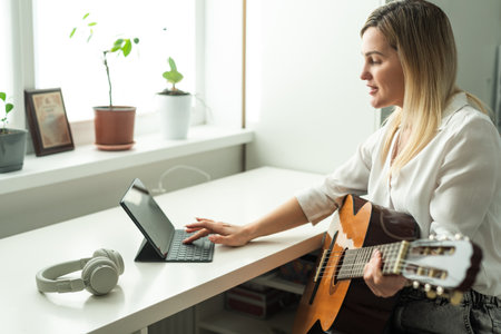 Woman artist playing the guitar and live or stream on laptop in the living room, Relaxation with music therapy, Provide enjoyment and entertainment to viewers or fan clubs, Music, Acoustic guitar.の写真素材