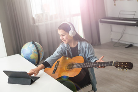 Latin girl with headphones listening to her online music lessons. Artistic kid playing the acoustic guitar and learning the chordsの写真素材