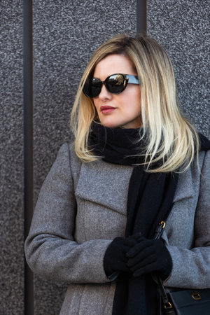 Beautiful young stylish blonde woman wearing long coat walking through the city streets. Trendy casual outfit. Street fashion.の写真素材
